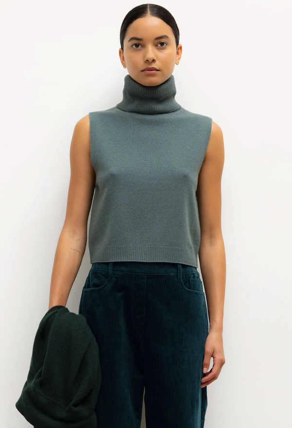 Woman wearing a sleeveless green turtleneck top against a white background