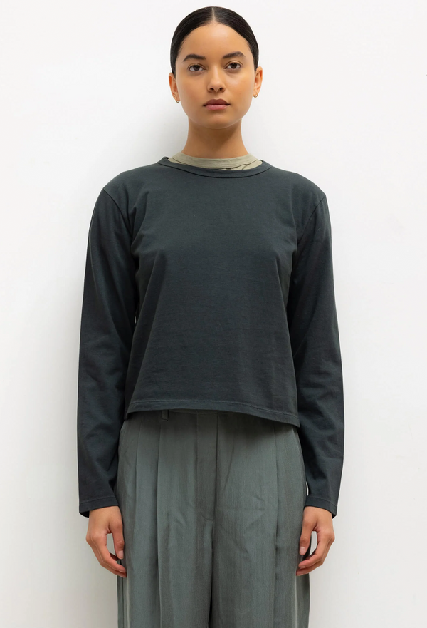 Person wearing a dark green long-sleeve top and gray pants on a white background