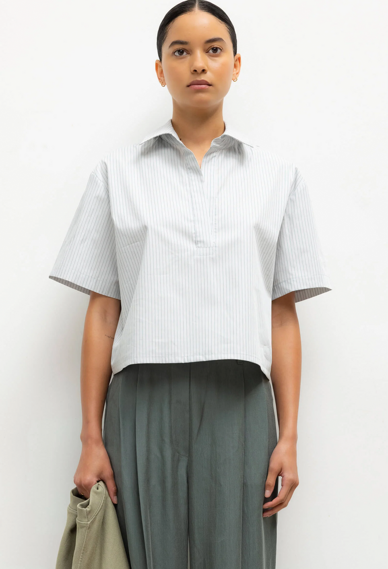 Person wearing a light-colored striped short-sleeve shirt and gray pants against a white background