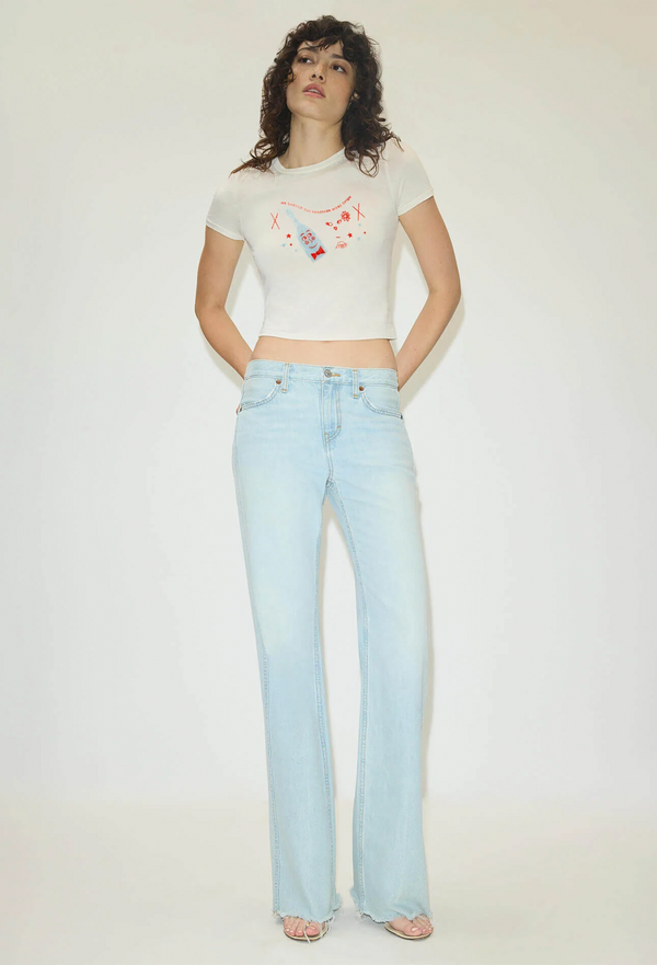 Woman wearing a white t-shirt with colorful graphics and light blue jeans on a plain background