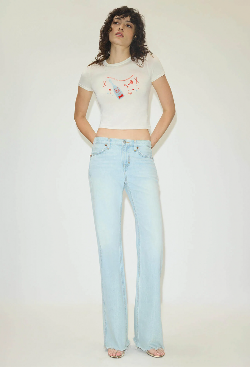 Woman wearing a white t-shirt with colorful graphics and light blue jeans on a plain background