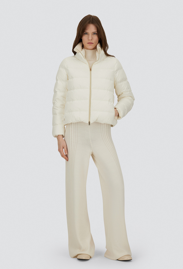 Person wearing a cream puffer jacket and pants on a white background