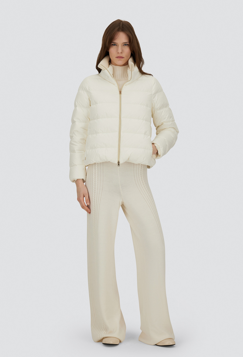 Person wearing a cream puffer jacket and pants on a white background