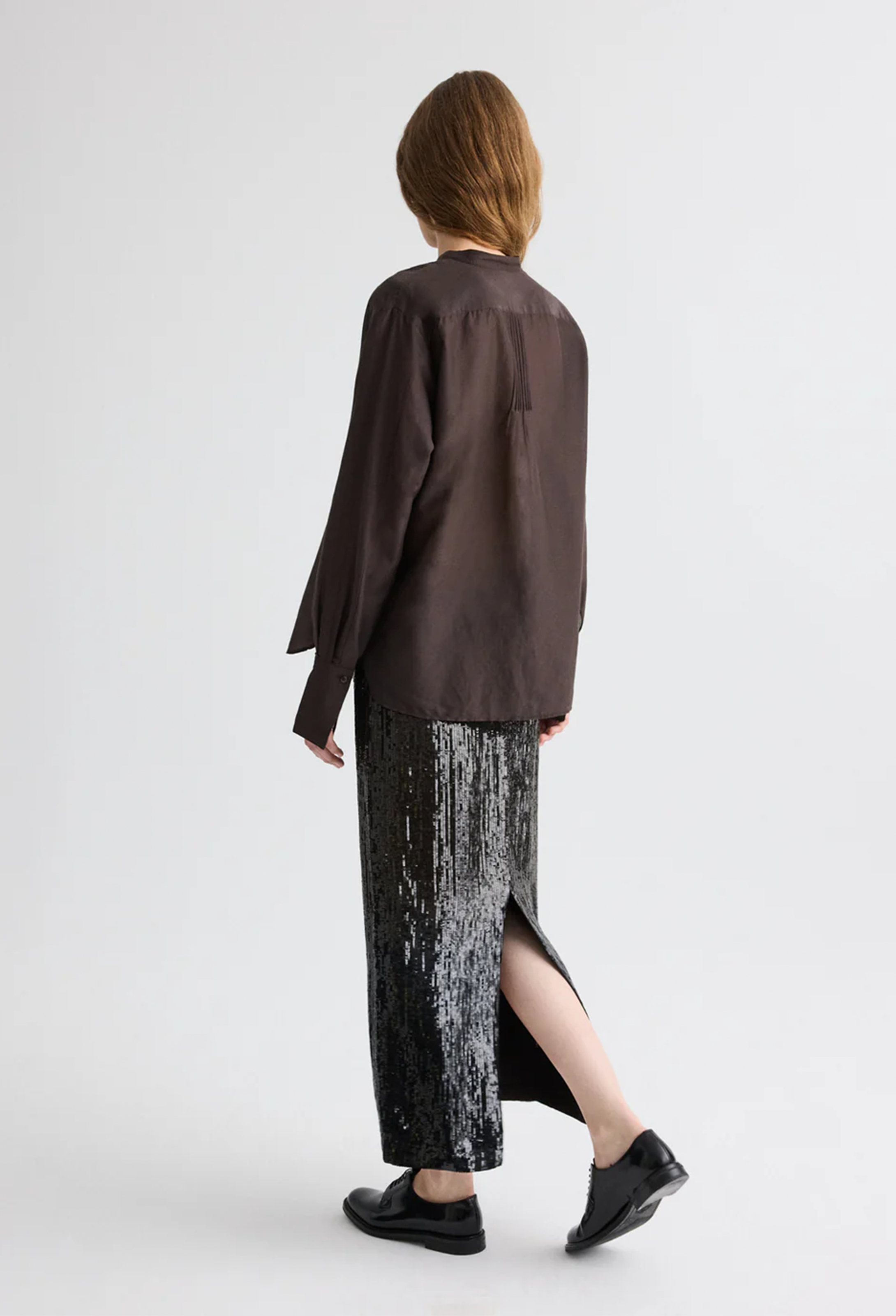 Person wearing a brown long-sleeve shirt and black patterned skirt on a white background
