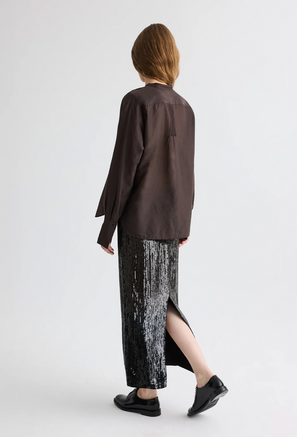 Person wearing a brown long-sleeve shirt and black patterned skirt on a white background