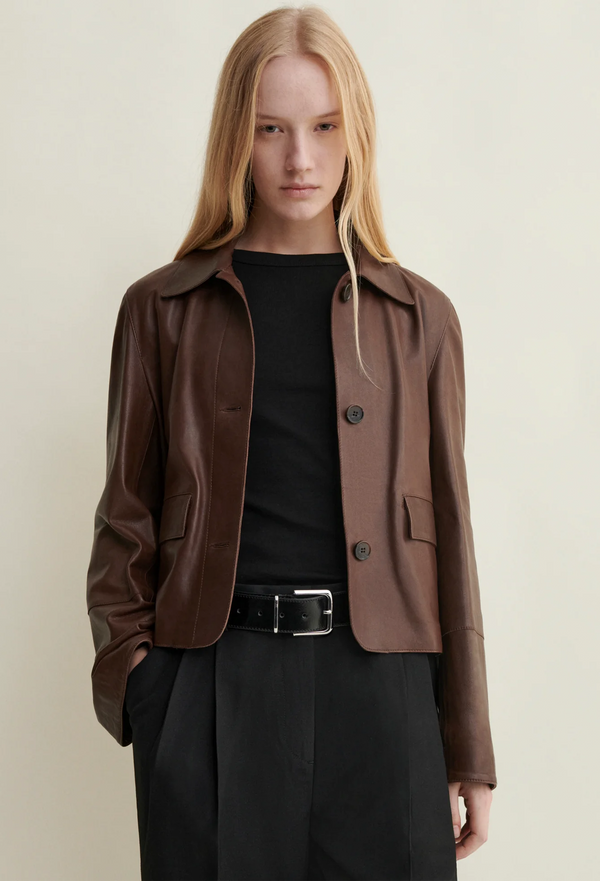 Person wearing a brown jacket over a black top and pants on a beige background