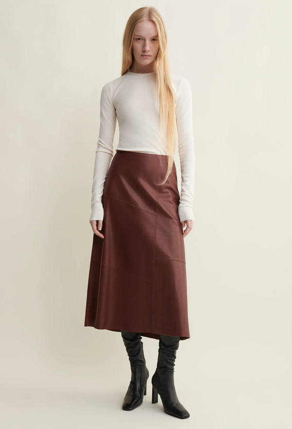 Woman wearing a white top and brown skirt with black boots on a plain background