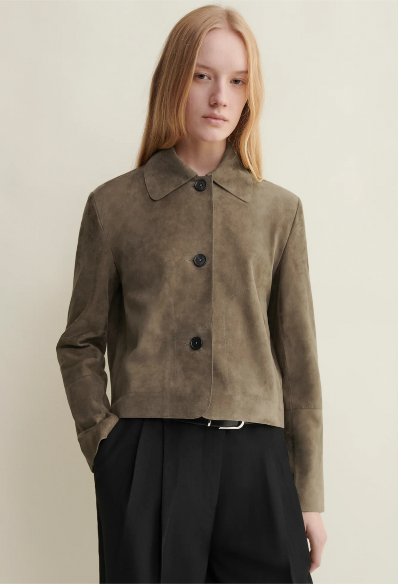 Person wearing a brown suede jacket with black buttons on a plain background