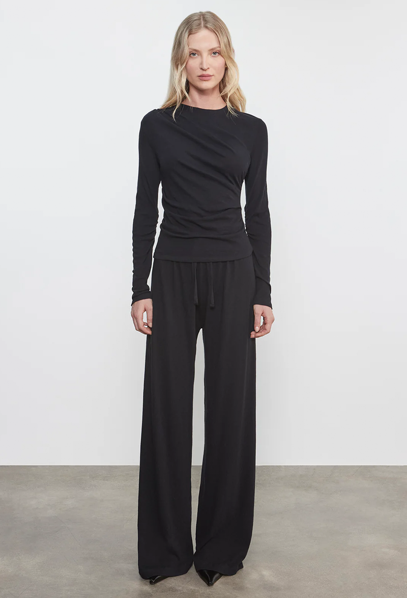 Woman wearing a black long-sleeve top and wide-leg pants against a white background