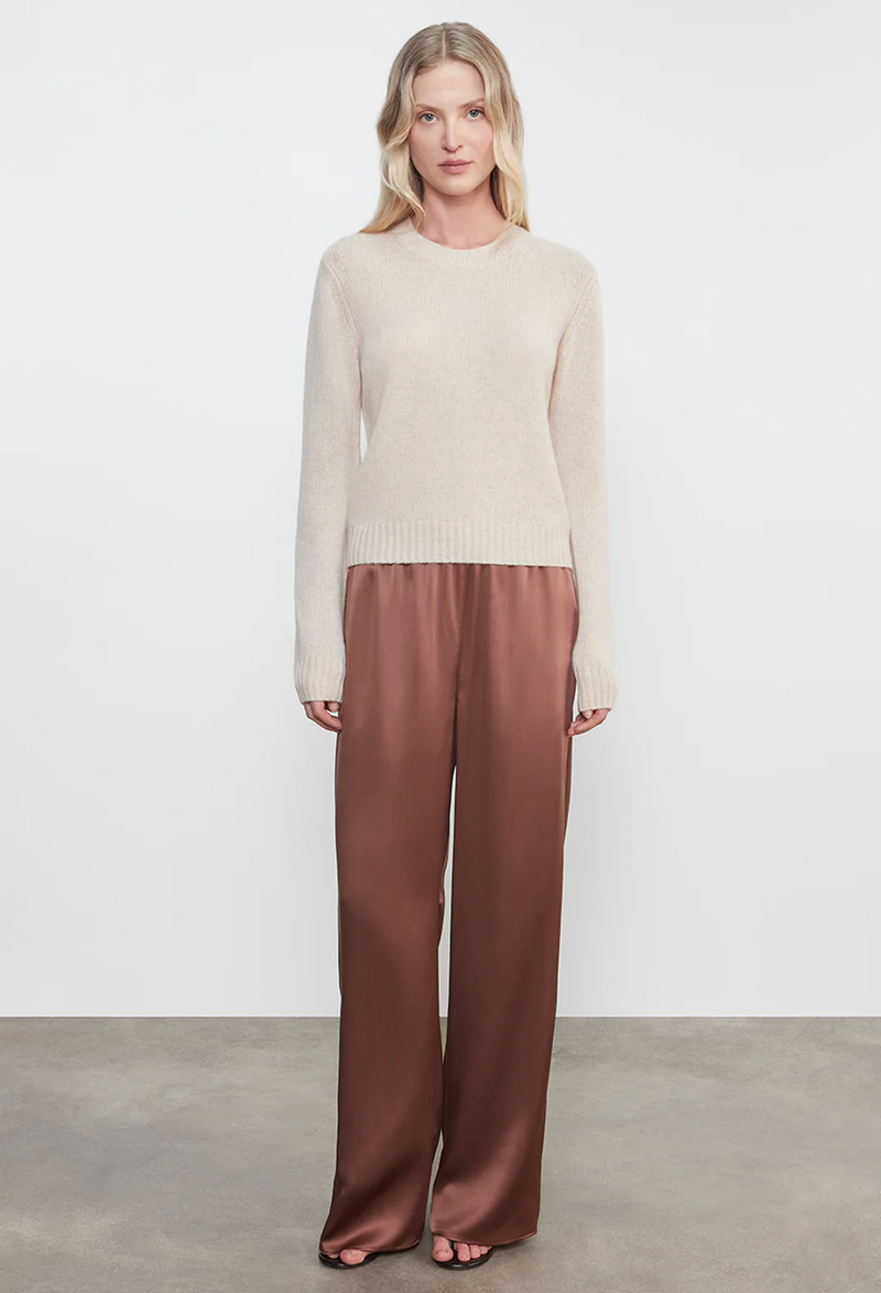 Woman wearing a cream sweater and brown pants on a white background
