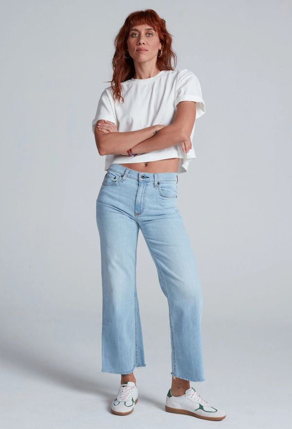 Woman wearing a white t-shirt and light blue jeans against a plain background
