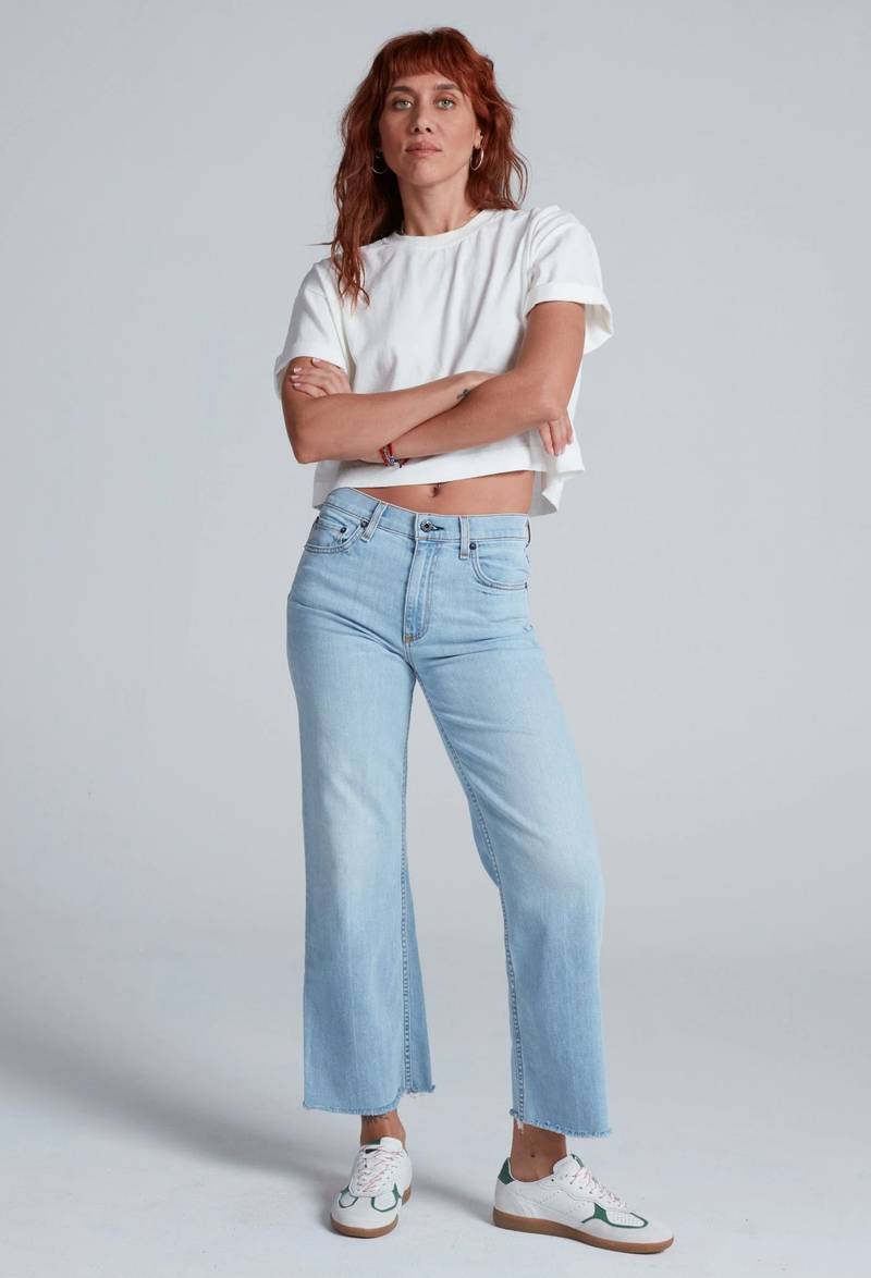 Woman wearing a white t-shirt and light blue jeans against a plain background