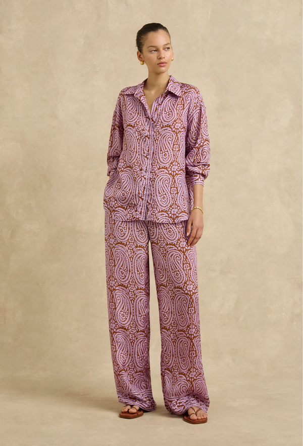 Person wearing a pink paisley shirt and pants set against a beige background