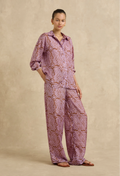 Woman wearing a pink paisley shirt and pants set against a beige background