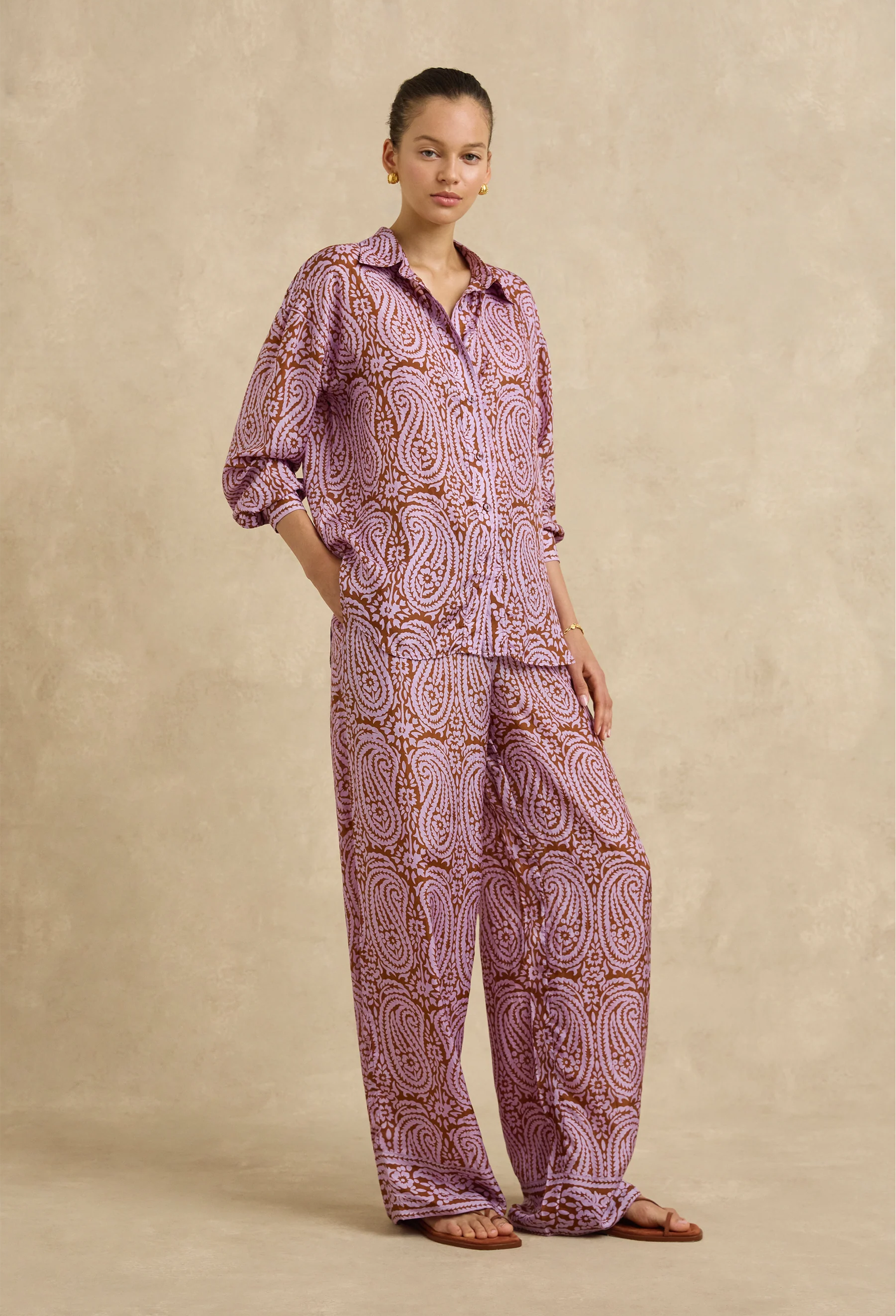 Woman wearing a pink paisley shirt and pants set against a beige background