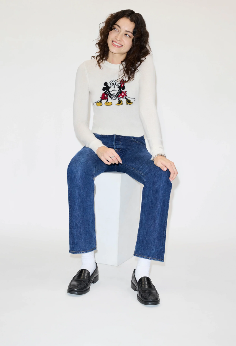 a model wearing a mickey mouse cashmere crewneck and jeans on a white background