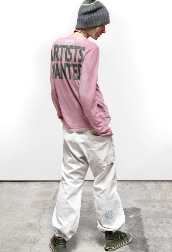 a model wearing a pink long sleeve tee with ARTISTS WANTED on the back