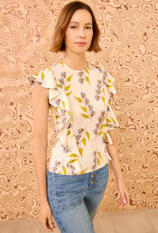 Woman wearing a floral blouse and jeans against a patterned wall.