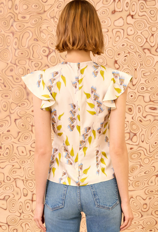 Person wearing a floral blouse with ruffled sleeves against a patterned wall.
