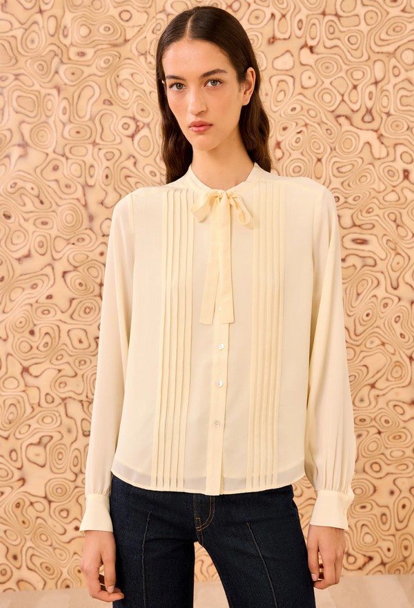 Woman wearing a cream blouse with a bow tie against a patterned beige background