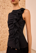 Black ruffled top worn by a model against a patterned wall.
