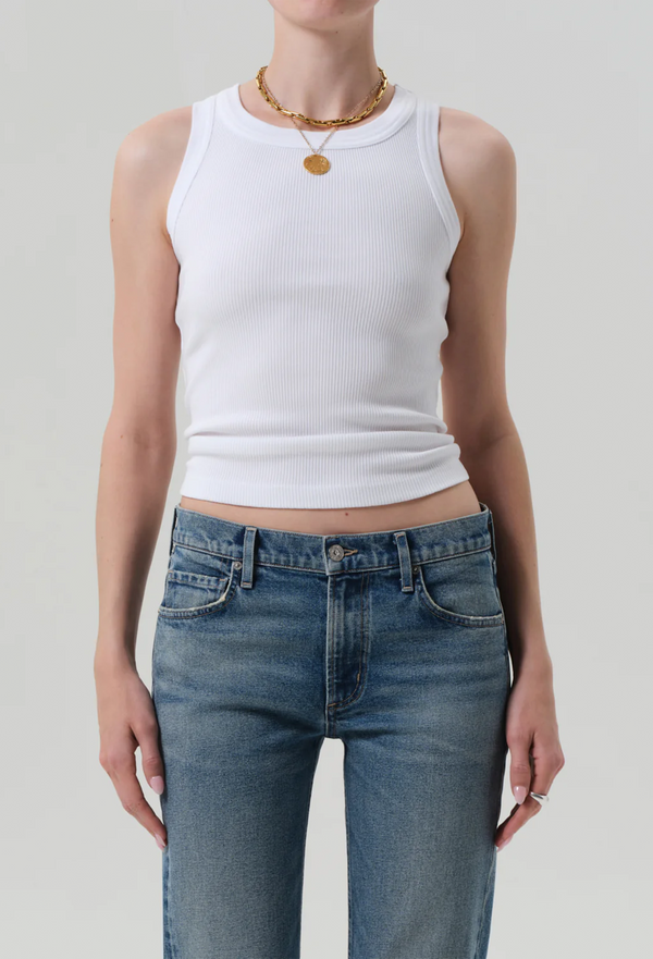 Person wearing a white sleeveless top and blue jeans on a plain background