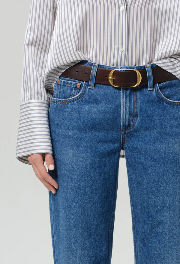 Person wearing blue jeans with a brown belt and striped shirt on a light gray background