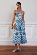 Woman wearing a blue floral dress standing against a white wall.