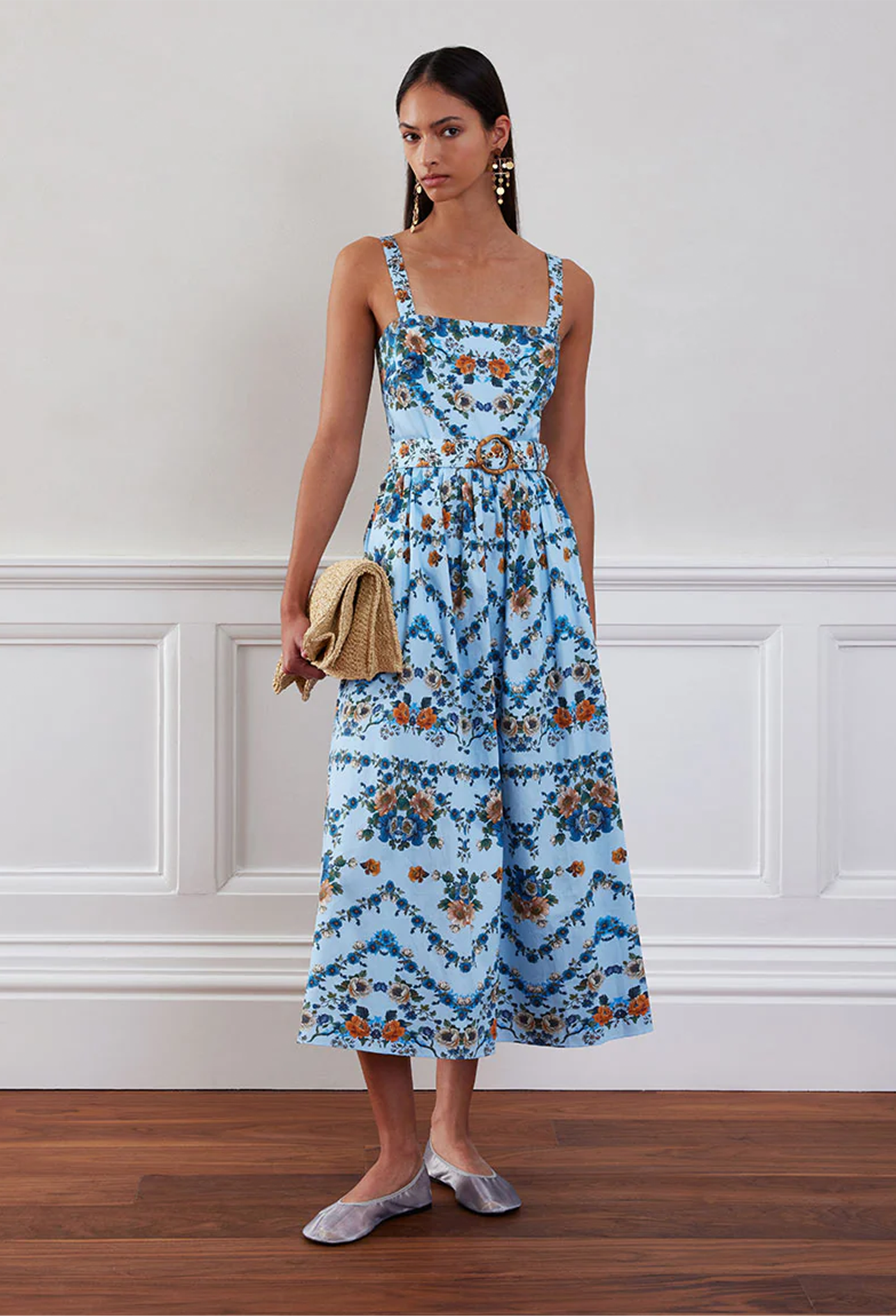 Woman wearing a blue floral dress standing against a white wall.