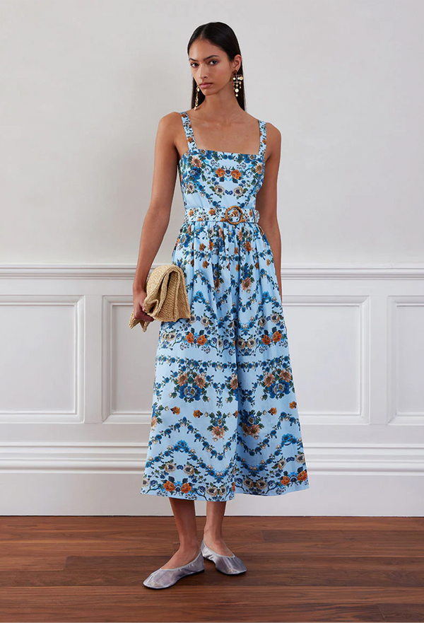 Woman wearing a blue floral dress standing against a white wall.