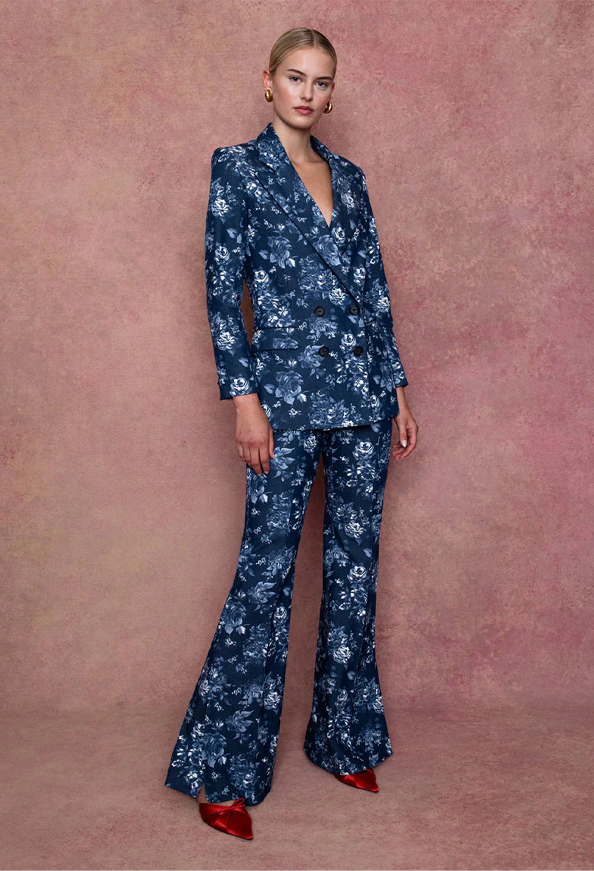 Woman wearing a blue floral suit with red shoes against a pink background