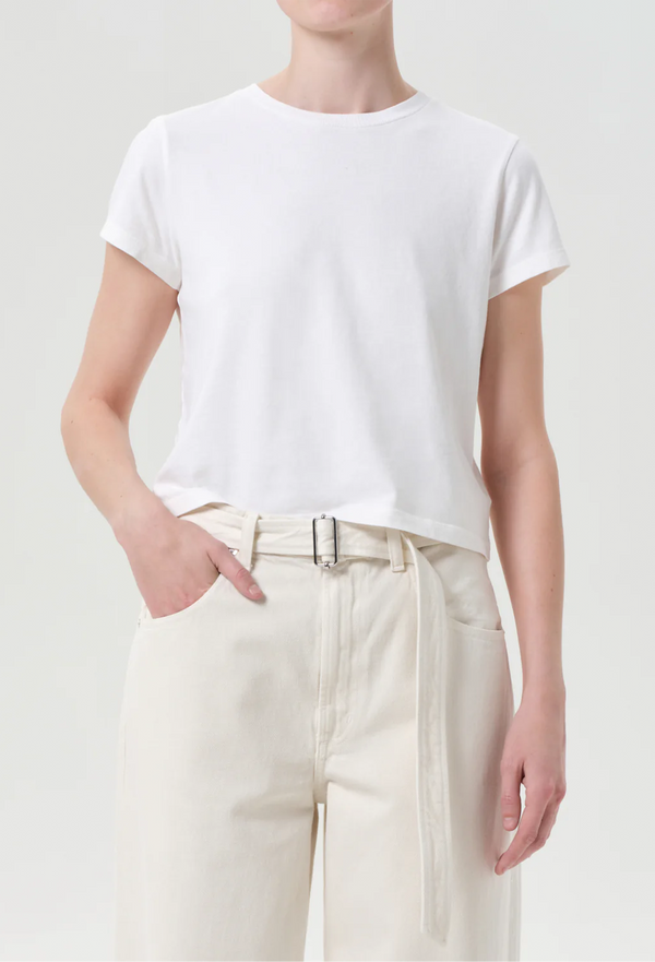 Person wearing a plain white t-shirt and light-colored pants on a neutral background