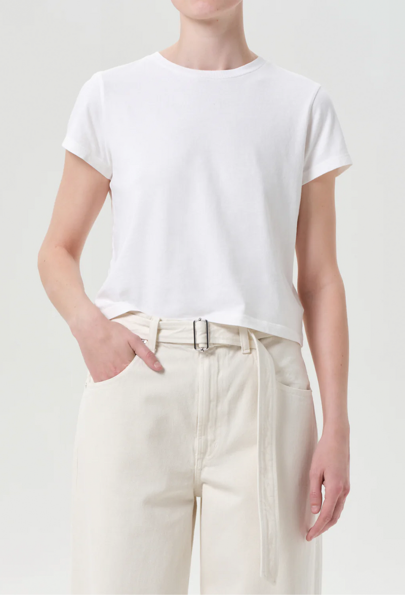 Person wearing a plain white t-shirt and light-colored pants on a neutral background