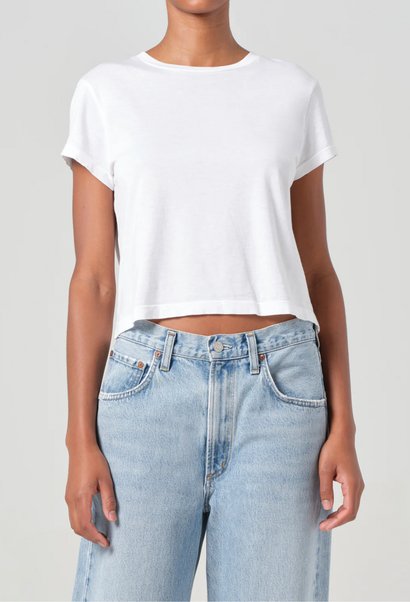 Person wearing a white crop top and light blue jeans on a plain background
