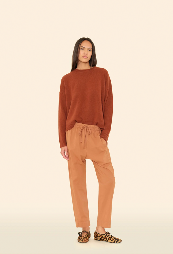 Woman wearing a brown sweater and tan pants on a beige background