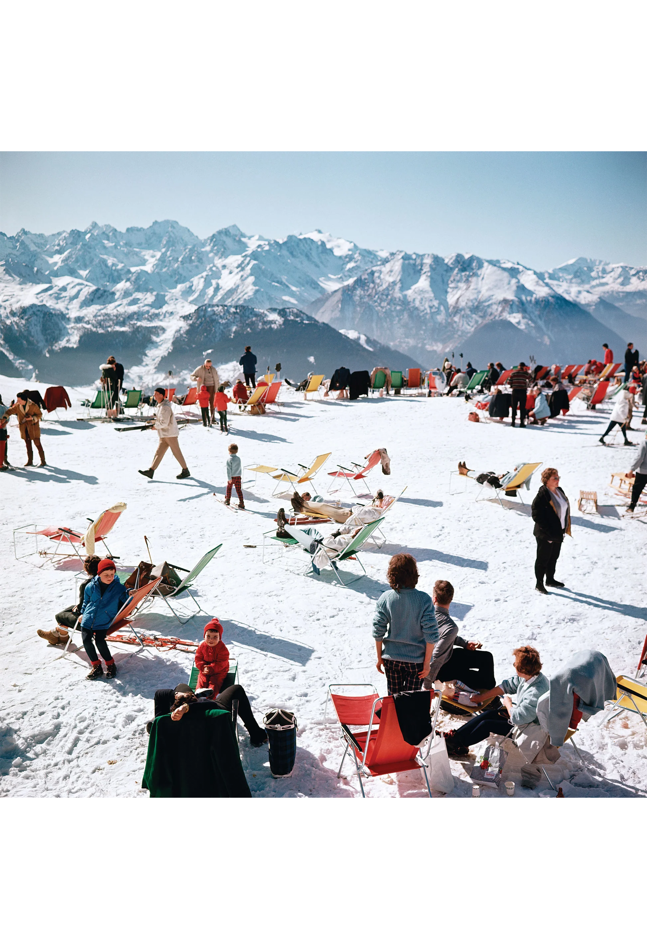 People enjoying a snowy mountain top with colorful chairs and mountains in the background