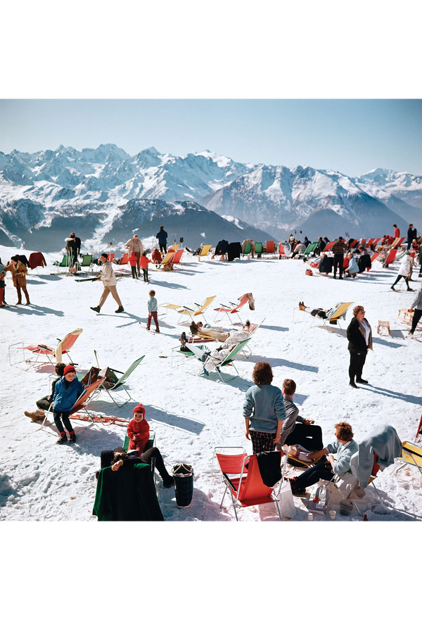 People enjoying a snowy mountain top with colorful chairs and mountains in the background
