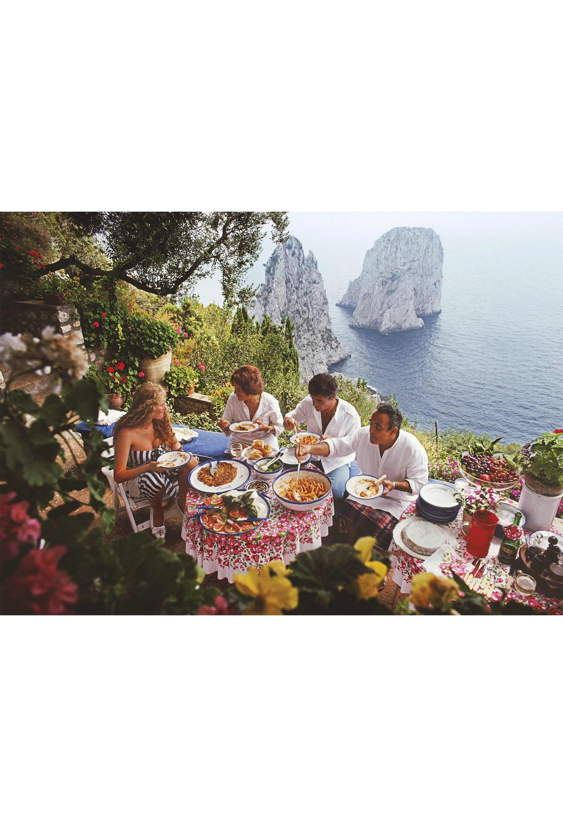 People dining outdoors with scenic ocean view and rock formations.