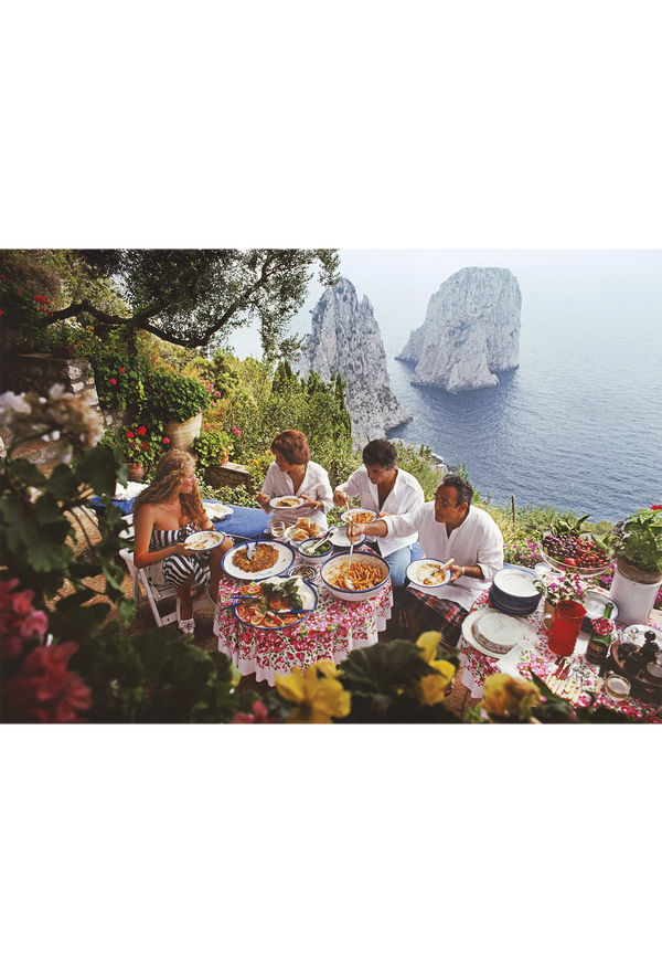 People dining outdoors with scenic ocean view and rock formations.