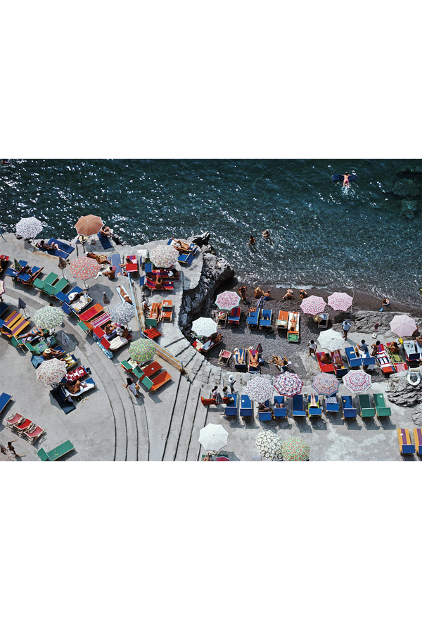 A scenic view of a coastal area with people, colorful chairs, and umbrellas by the water.