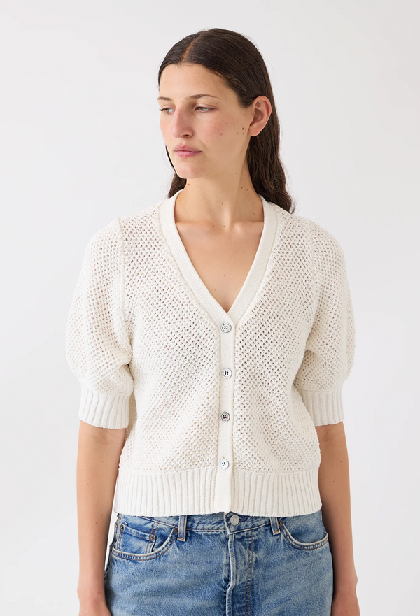 Woman wearing a white textured cardigan and blue jeans against a white background