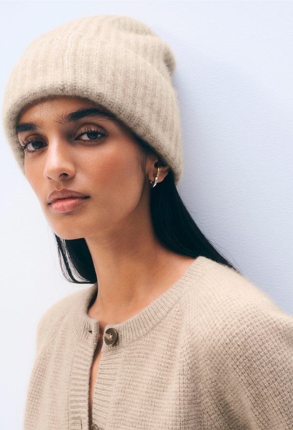 Woman wearing a beige knit hat and cardigan against a light blue background