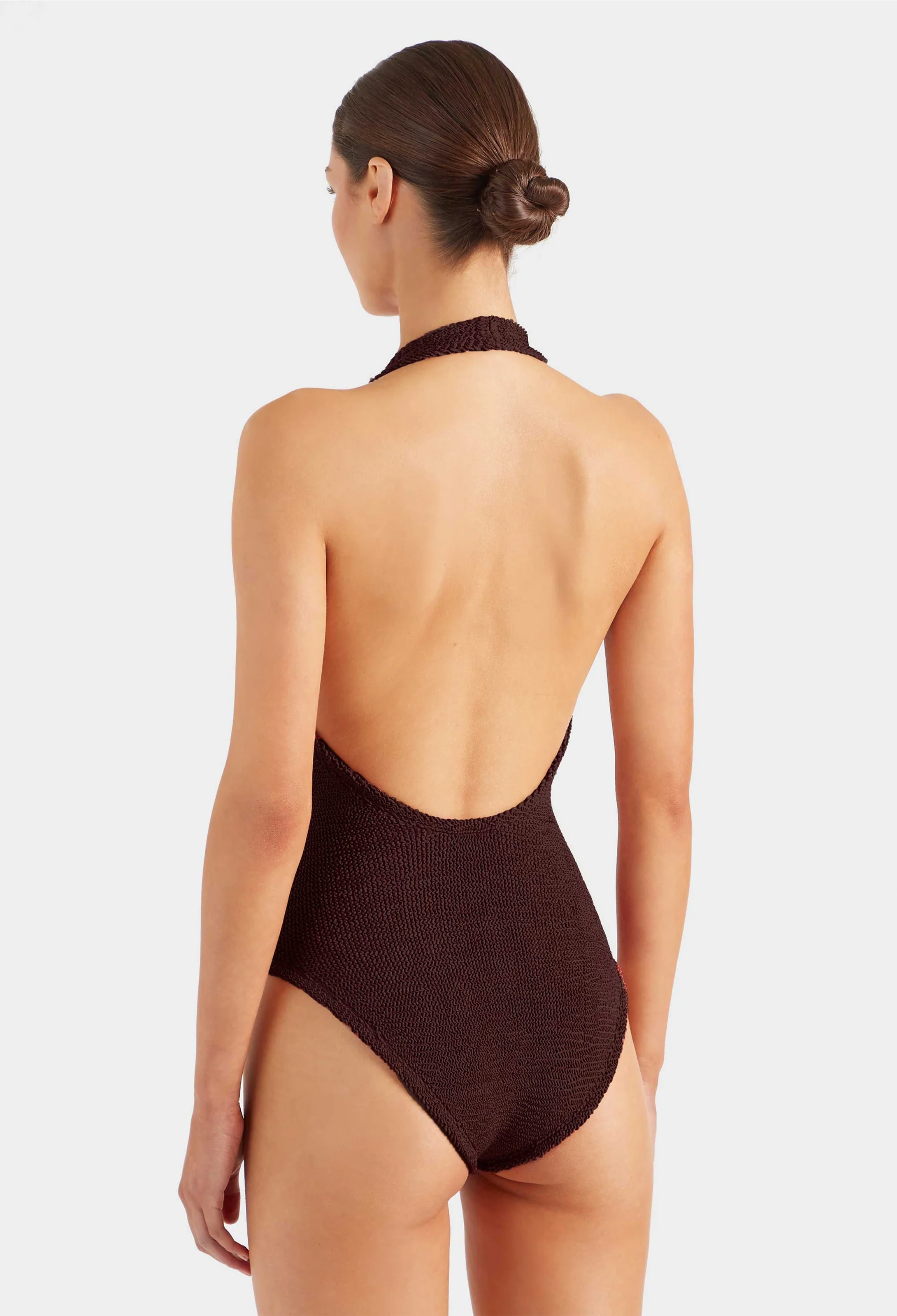 Woman wearing a brown swimsuit with a halter neck design on a white background
