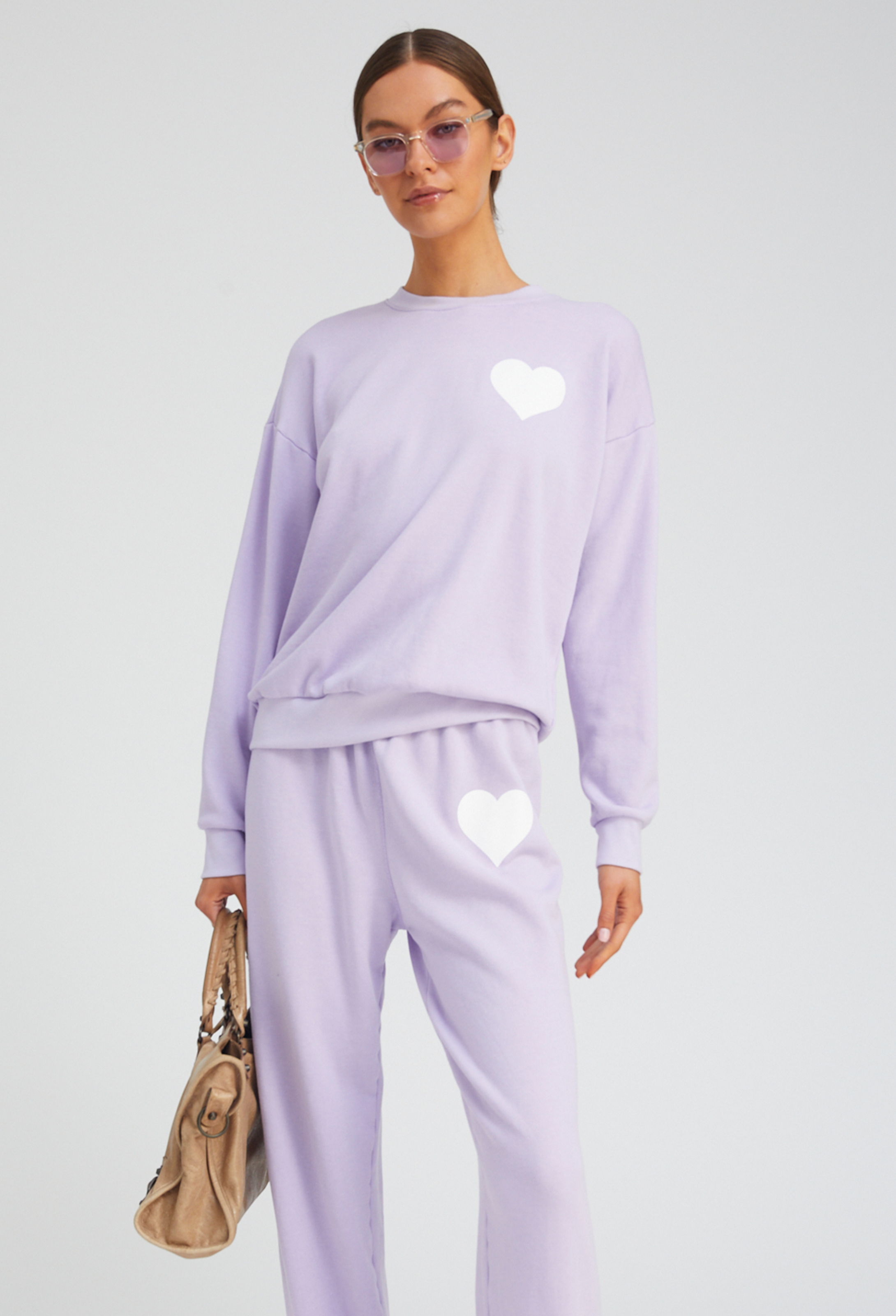 Person wearing a lavender tracksuit with heart designs on a light gray background