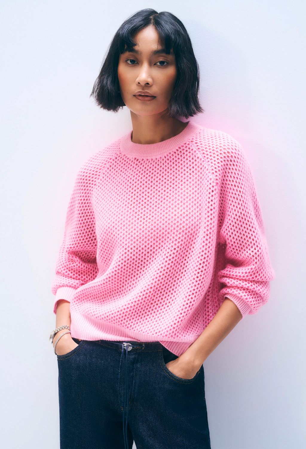 Person wearing a pink mesh sweater against a plain background