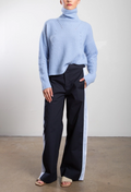 Person wearing a light blue ribbed sweater and black pants on a plain background