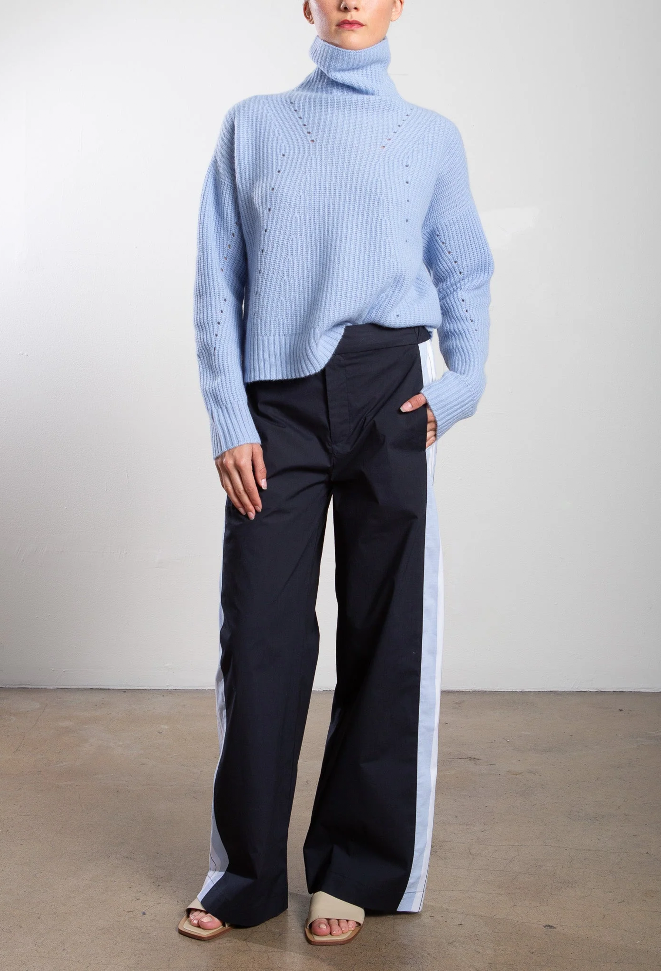 Person wearing a light blue ribbed sweater and black pants on a plain background