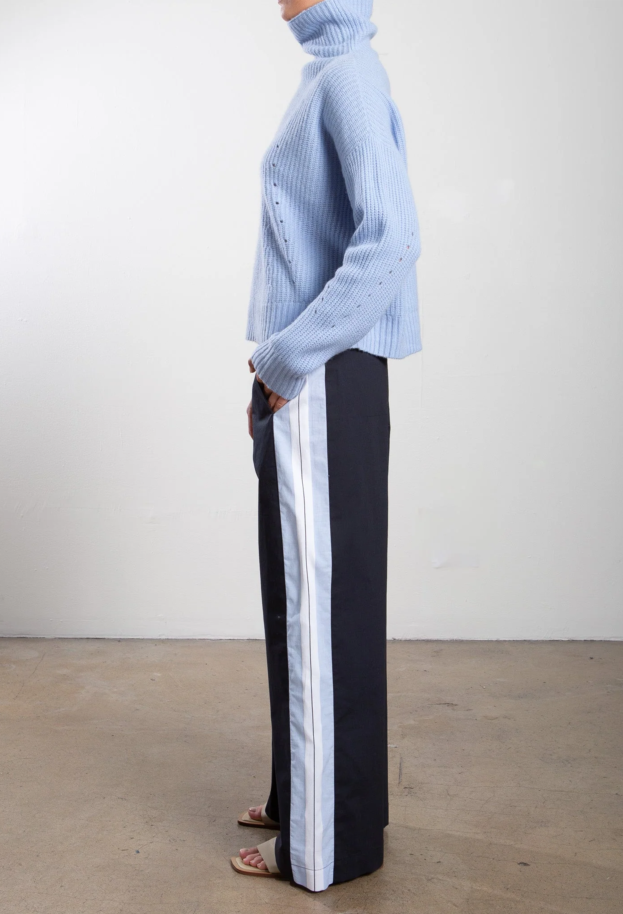 Person wearing a light blue sweater and black pants with white stripes on a plain background