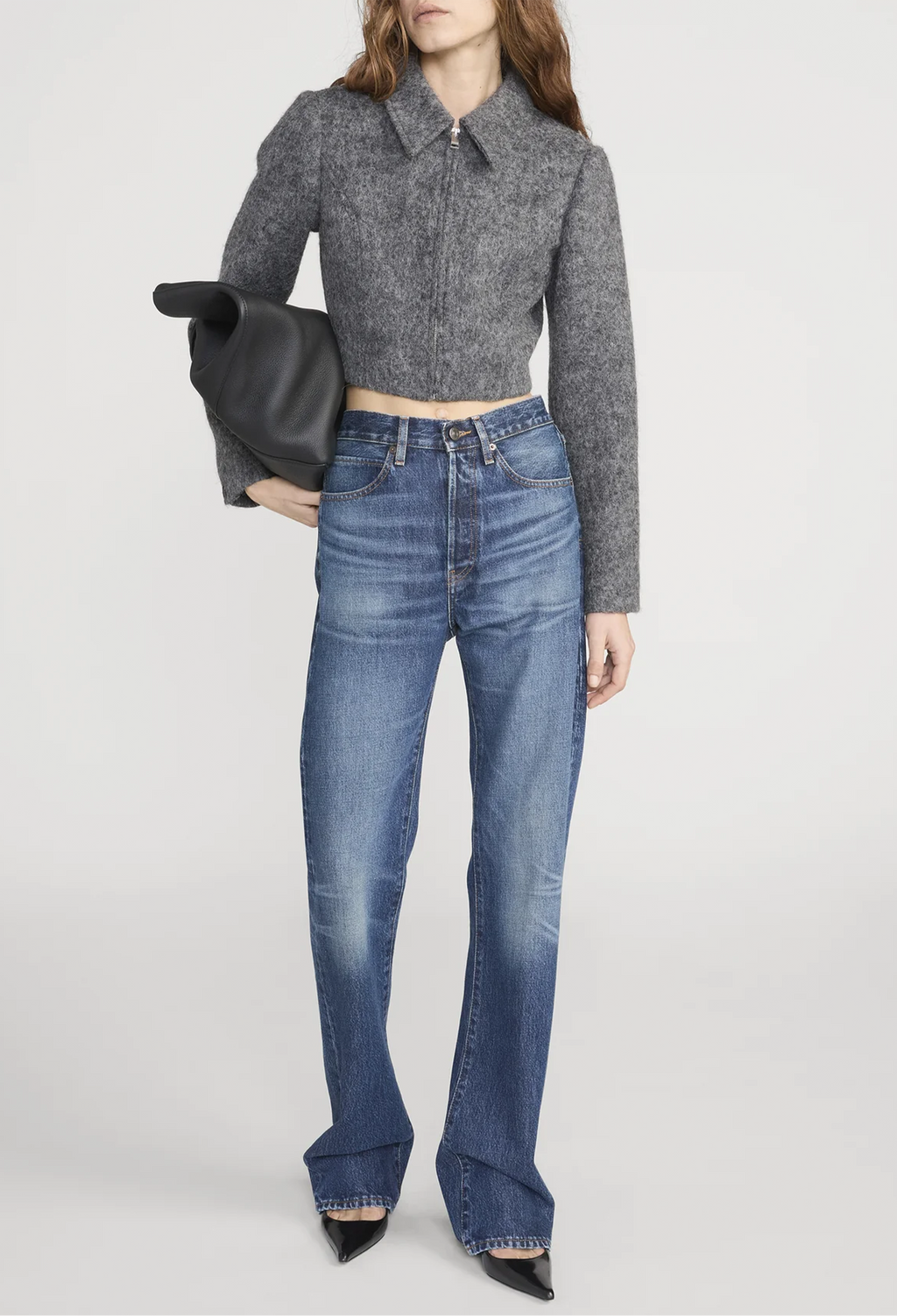 Person wearing a gray cropped sweater and blue jeans on a white background