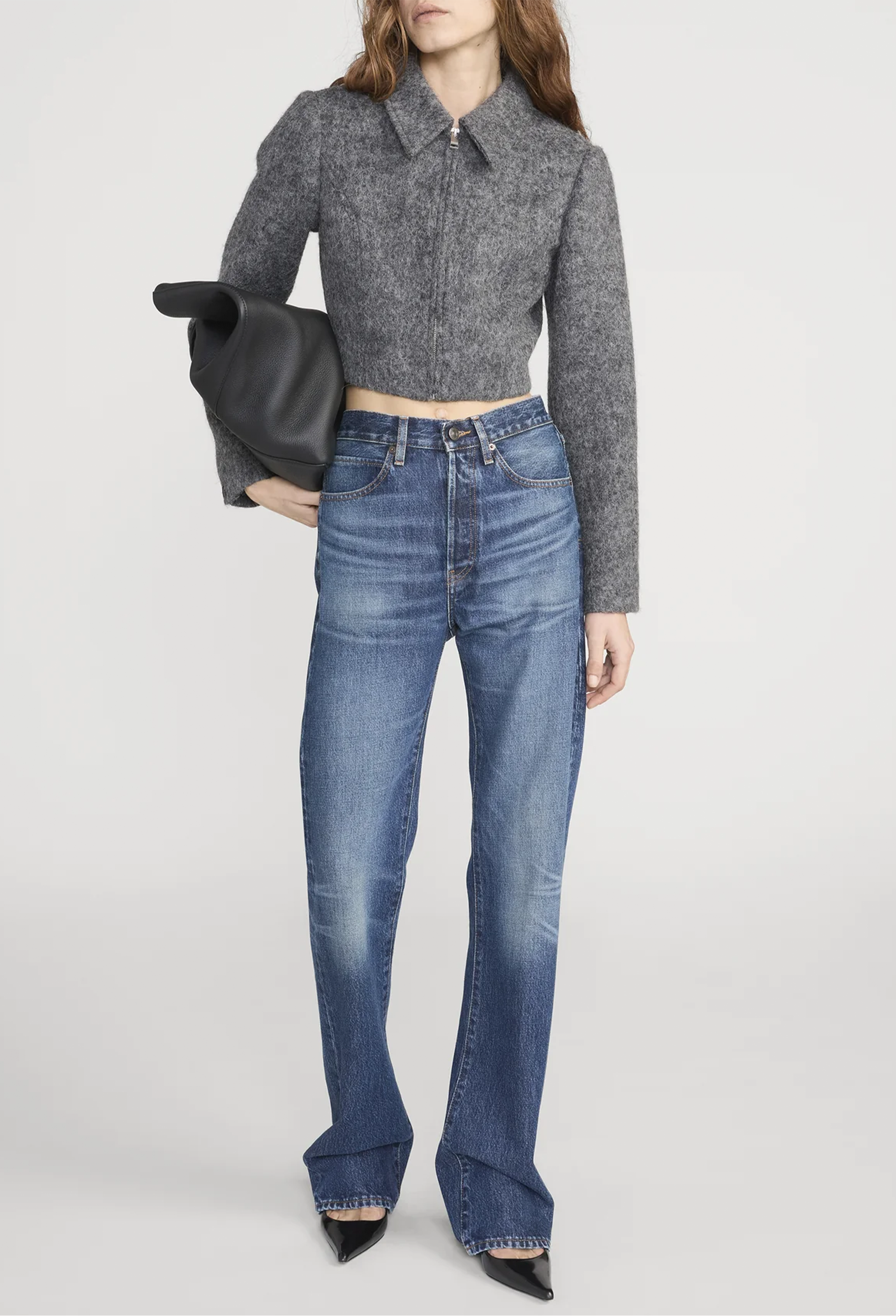 Person wearing a gray cropped sweater and blue jeans on a white background